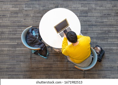 A Man Sitting In A Breakroom Is Using A Cellphone And A Computer