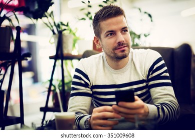 Man Sitting At Cafe With Smart Phone In His Hands. Shallow Depth Of Field.