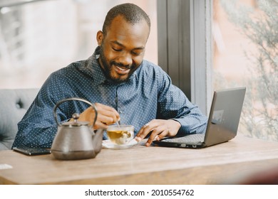 Man Sitting In A Cafe And Working Behind A Laptop, Writing In A Notebook And Drink A Tea.