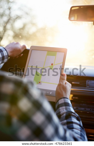 Man sitting in car and holding tablet with map\
gps navigation, toned at\
sunset.