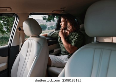 Man sitting in car looking out of the window, deep in thought, surrounded by nature - Powered by Shutterstock