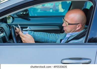 Man Sitting In Car With Mobile Phone In Hand Texting While Driving. Distracted Guy Checking His Smart Phone Not Paying Attention Reading Text Message Email Outdoors Background