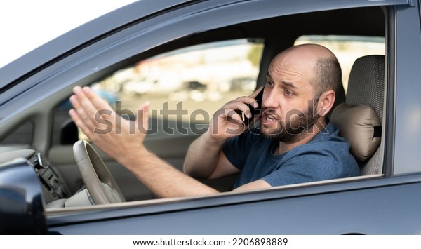 Man sitting in car with\
mobile phone calling while driving. Distracted shocked guy not\
paying attention at road using smartphone annoyed by bad news\
outdoors background