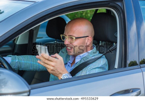 Man\
sitting in car with mobile phone in hand texting while driving.\
Distracted guy checking his smart phone not paying attention\
reading text message email outdoors\
background