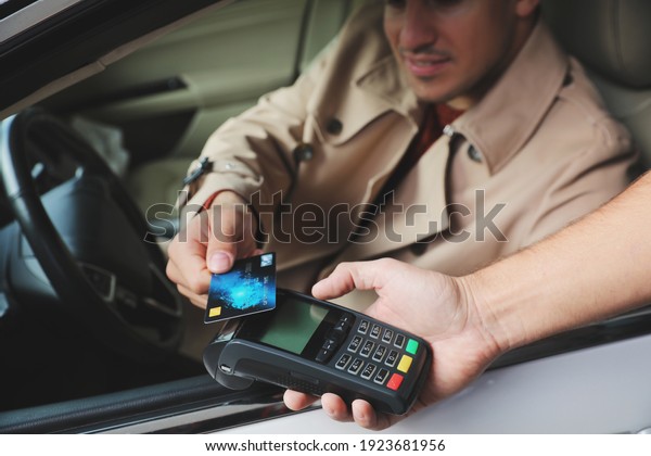 Man sitting in car and paying with credit card at\
gas station, closeup