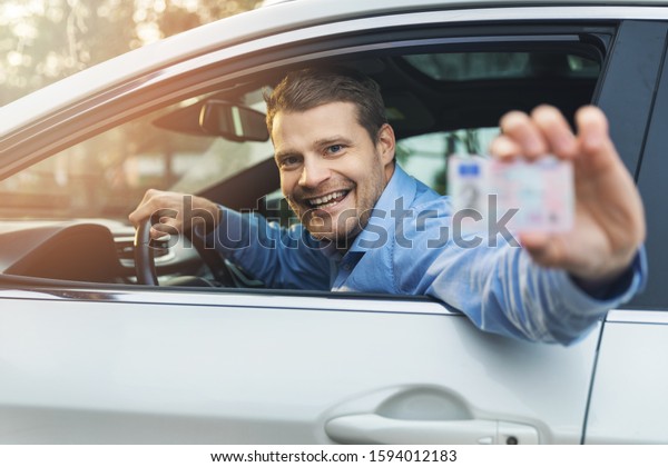 man sitting in the car and showing his driver\
license out of car window