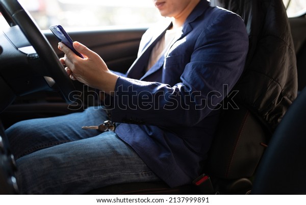 Man sitting in car using mobile phone to text\
while driving. Close-up of businessman while driving typing message\
on mobile phone.
