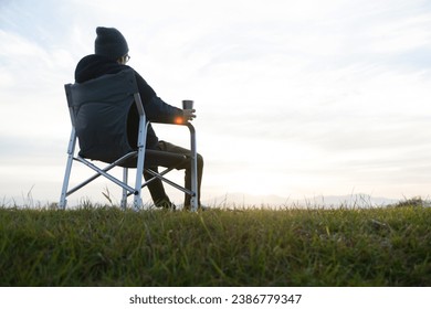 a man is sitting in a chair, sipping coffee, and gazing at the sunrise - Powered by Shutterstock