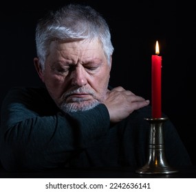 A man is sitting in the dark next to a burning candle and has fallen asleep. The background is black. - Shutterstock ID 2242636141