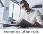 Man sitting at desk in the office and reading a newspaper, he is focused and thinking