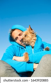 Man Sitting With Dog In Matching Blue Hooded Sweatshirts Under Bright Blue Sky