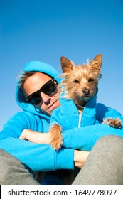 Man Sitting With Dog In Matching Blue Hooded Sweatshirts Under Bright Sunny Sky