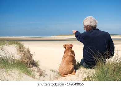 Man Sitting With Dog On Sand Dune At Dutch Beach On Wadden Island Texel