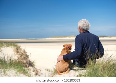 Man Sitting With Dog On Sand Dune At Dutch Beach On Wadden Island Texel