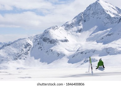 Man sitting down on a slope next to his skis facing a huge snow mountain. - Powered by Shutterstock