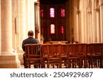 Man Sitting in Empty Church with Stained Glass Windows and Wooden Pews.