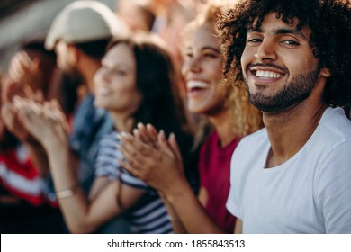 Man Sitting With Friends Watching A Soccer Match And Applauding At Stadium. Group Of Young People Watching A Football Game.