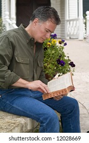 A man sitting in front of the entrance to a church building studying from his bible.