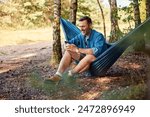 Man sitting in hammock using mobile phone in forest