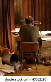 Man Sitting At His Desk In A Messy Apartment.