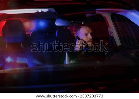 man sitting inside a car and talking on the phone after being stopped by police at night