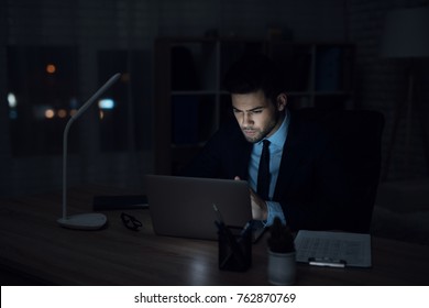 A Man Is Sitting At A Laptop In A Dark Office. The Man In The Suit Works Until Late.