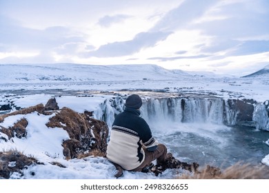 A man sitting looking at the frozen Godafoss waterfall at sunset in winter, Iceland - Powered by Shutterstock