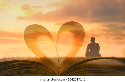 Man sitting looking out to the sunset against heart shape book page.  People, religion, searching for, love, wisdom, and knowledge concept. 