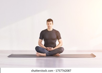 Man sitting at lotus yoga pose. Home morning routine. Teacher fitness studio. Asana class. Online exercise. Relaxation indoor. Male prayer in house room. Light background. Close eyes