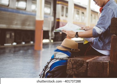 Man Sitting With Map. Travel Bag At The Train Station.vintage Filter Effected .