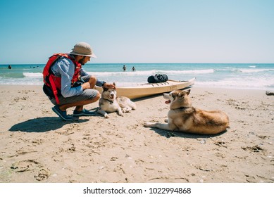 man sitting near the kayak boat with two siberian husky dogs on beach - Powered by Shutterstock