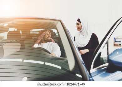 Man Is Sitting In New Car With Wife Standing Near Him. Arab Woman Looks At An Arab Man Who Is Sitting Inside A Car In A Car Dealership.