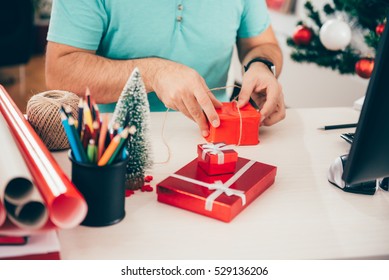 Man Sitting At The Office Desk And Wrapping Christmas Gifts