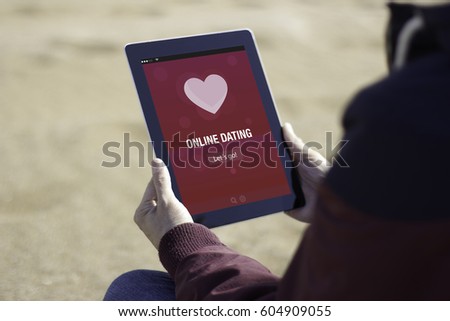Man sitting on the beach and using online dating app with his tablet 
