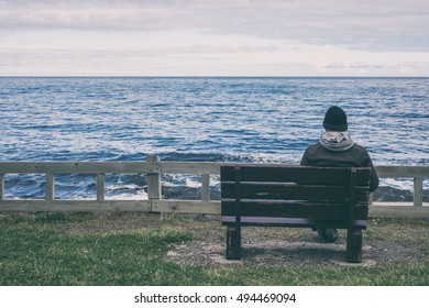 Man Sitting On Bench Overlooking Sea