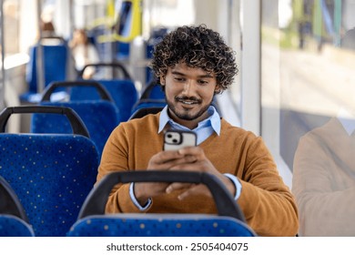 Man sitting on bus using smartphone with a smile. Casual setting in public transport with blue seats and window light. Engaged and relaxed moment captured.