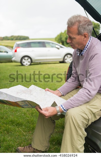 Man sitting on car boot
reading map