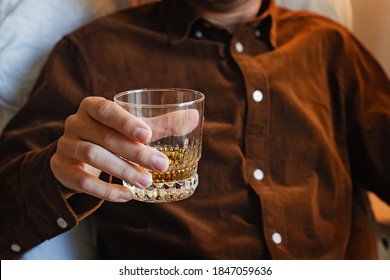 Man sitting on the chair and drinking whiskey. Close-up shot of the glass with bourbon, scotch or brandy