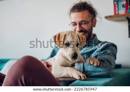 Man sitting on a chair at home and petting his adopted puppy dog. Focus on a dog sitting on a man lap. Life with pets. Copy space. .