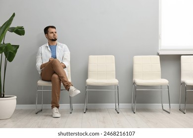 Man sitting on chair and waiting for appointment indoors - Powered by Shutterstock