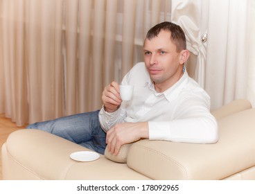 man sitting on the couch drinking a cup of coofee