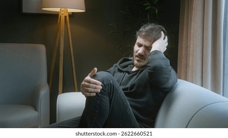 Man Sitting on Couch Holding His Head and Knee in Pain at Home