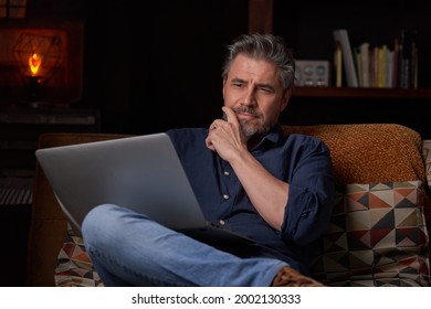 Man Sitting On Couch At Home With Laptop Computer. Businessman Working In Home Office. Portrait Of Mature Age, Middle Age, Mid Adult Man, Bearded, Thinking, Authentic Look.