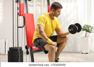 Man Sitting On A Fitness Machine And Exercising With A Dumbbell At Home Gym