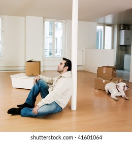 Man Sitting On The Floor Inside An Empty Loft Apartment With Tax Forms And Laptop Computer