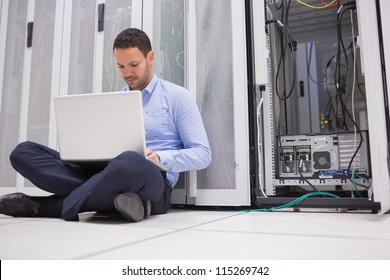 Man Sitting On Floor With Laptop Beside Servers In Data Center