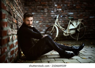 man sitting on floor outdoors with brickwall and bike in background