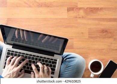 A Man Is Sitting On The Floor And Working On Laptop Over His Lap, Light From The Door. Top View With Copy Space.