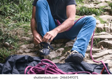 A man sitting on the ground puts on his climbing shoes. There is an out-of-focus climbing rope in the foreground which tells us that he is a climber getting ready to perform his favorite sport. - Powered by Shutterstock