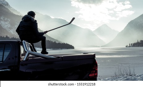 
Man sitting on the hood of a car. Hockey player looking for frozen pond. Shiny red pickup truck on ice covered road and snowy rural landscape. Offroad 4x4 - Powered by Shutterstock